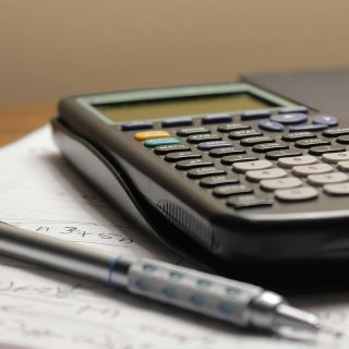 Calculadora e caneta apoiados sobre um documento com cálculos feitos a mão